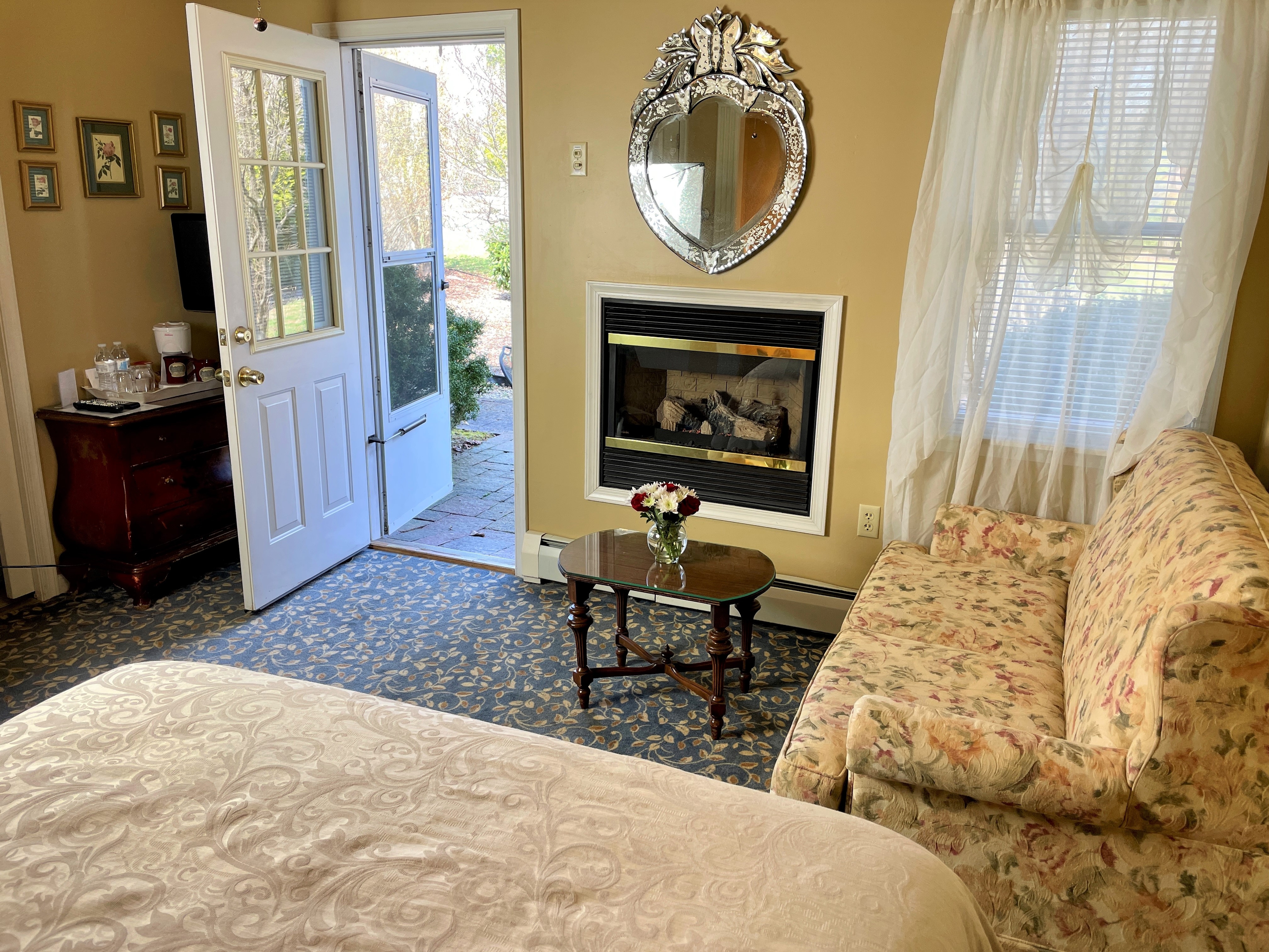 open door onto private patio and loveseat next to lit fireplace with cupcakes on a little table in front of fire