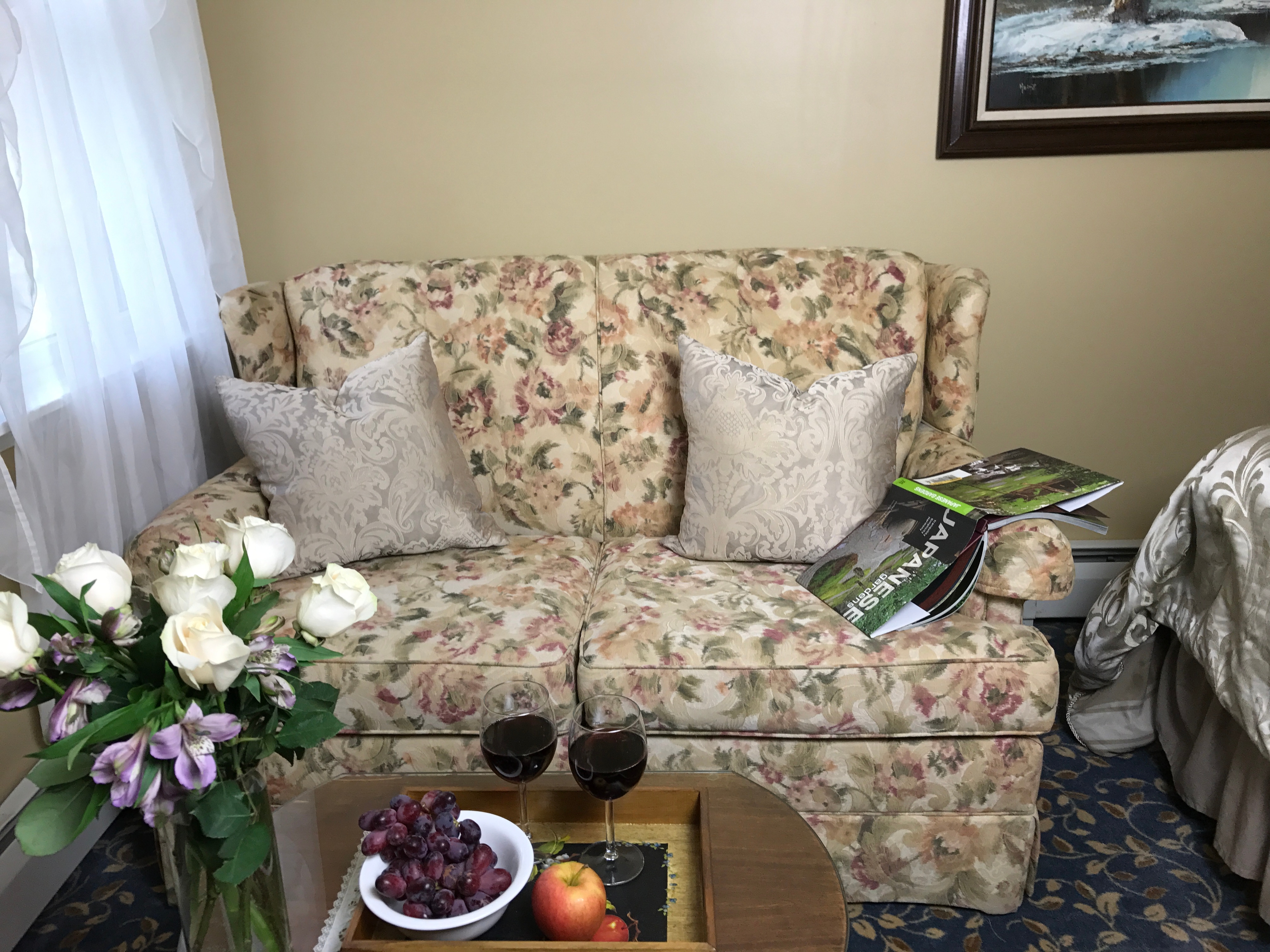 "Sitting area with love seat and coffee table with flowers, wine and fruit"