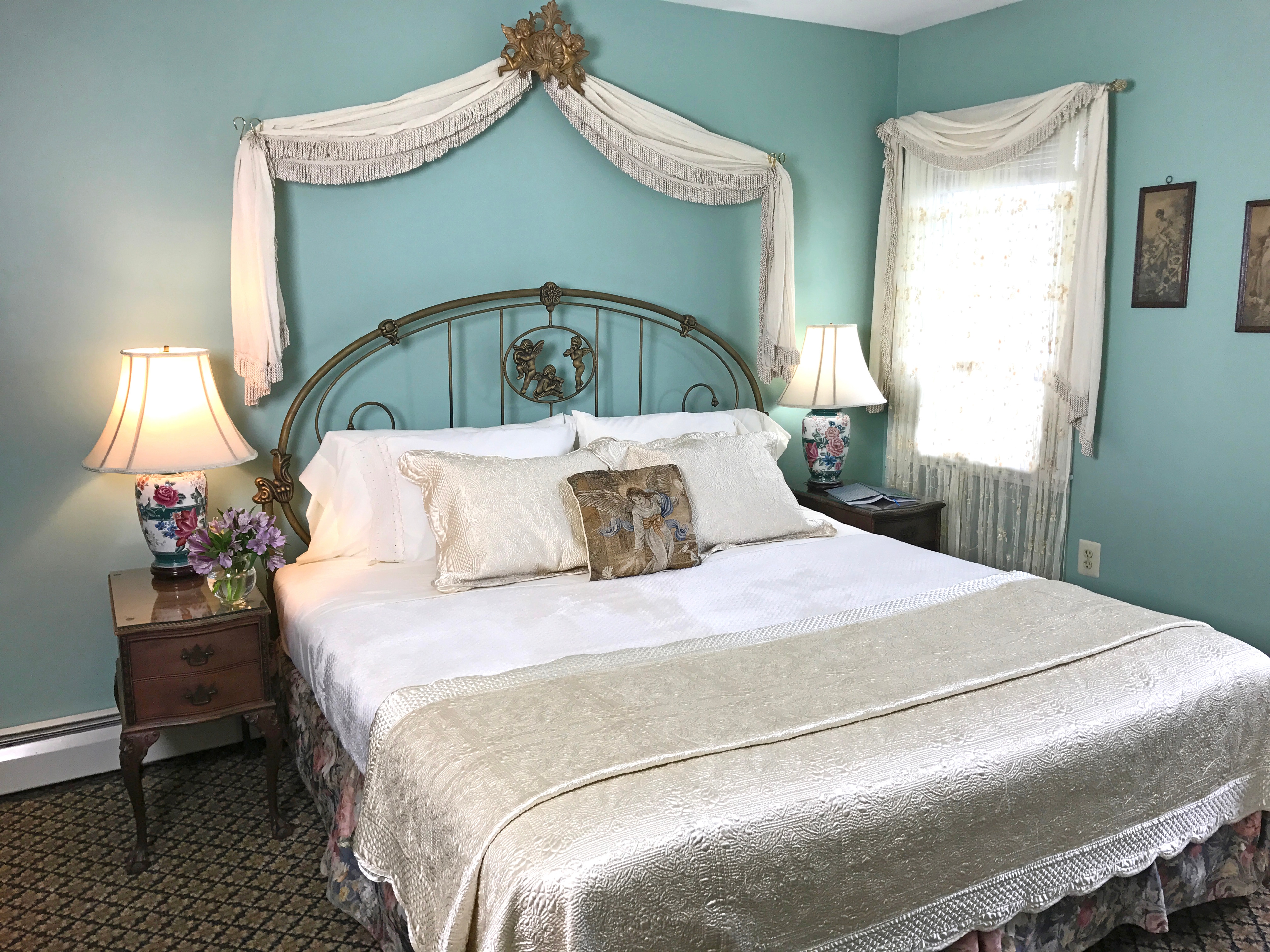 "Front view of king size bed with cherubs on headboard and  flower on nightstand"