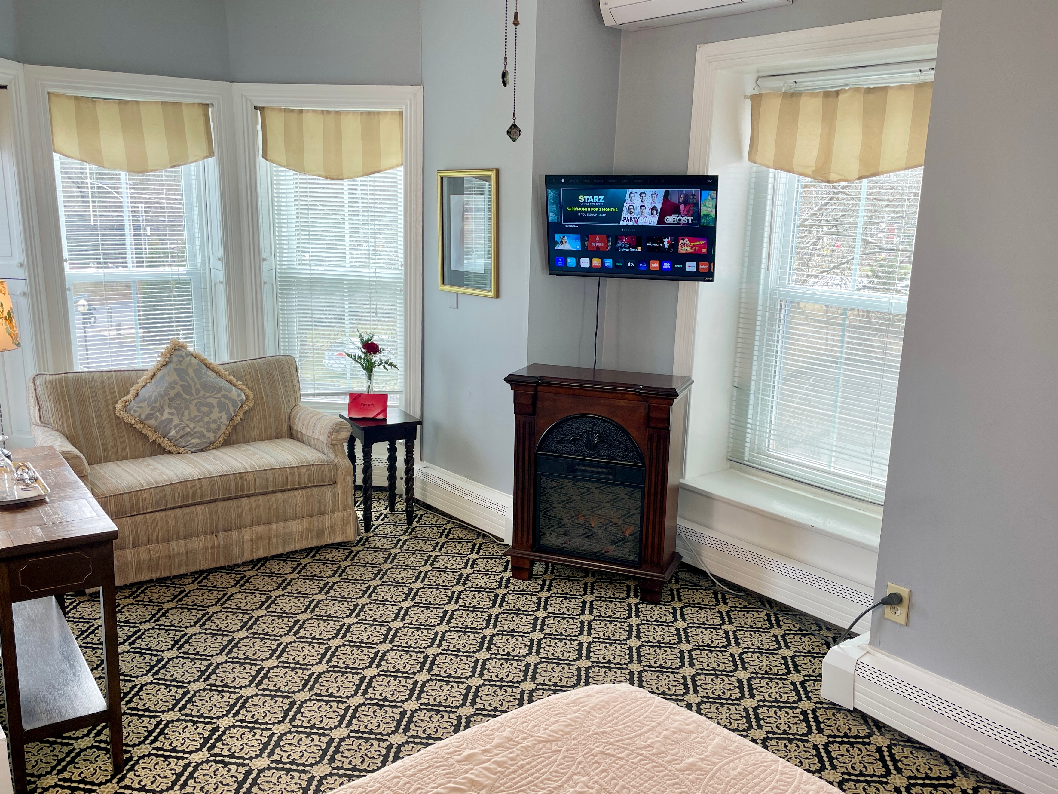 Sitting area of room in a sunny bay window with a large screen tv and a side table