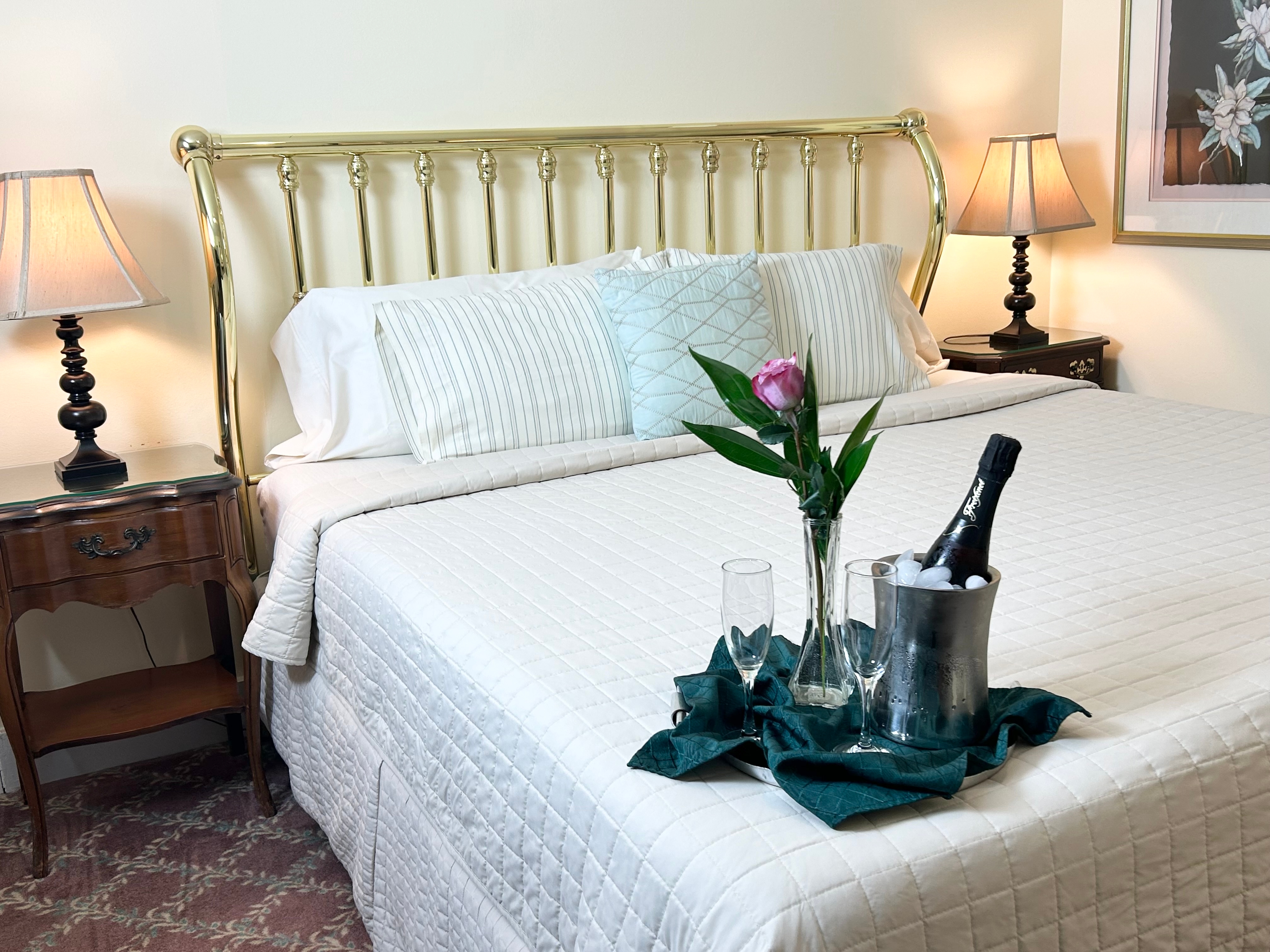 Beautiful King size bed and nightstands with a rose, champagne and champagne glasses on a tray and a picture of orchids on wall.