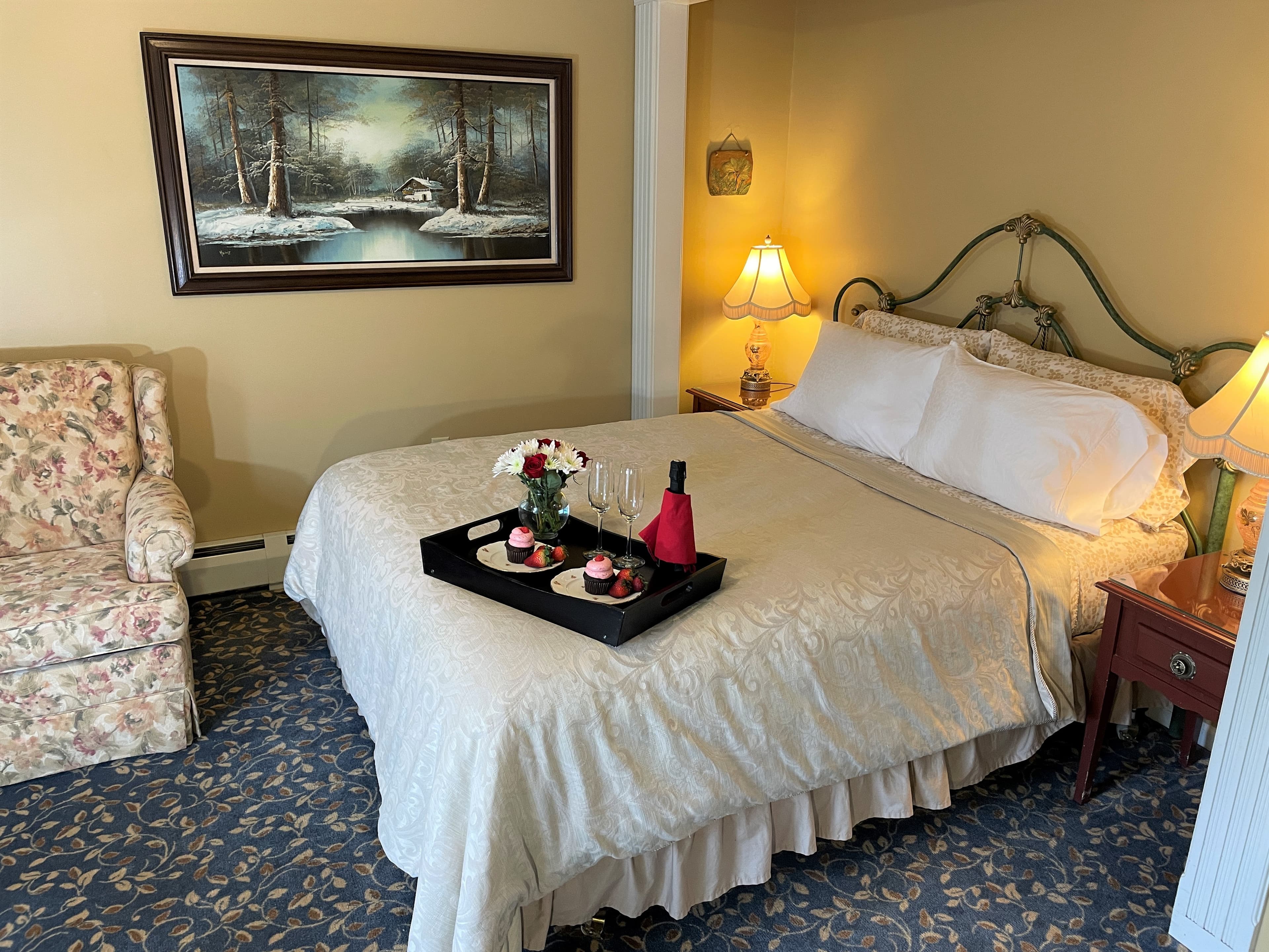 Queen bed with tray of pink and chocolate cupcakes, champagne, glasses and flowers