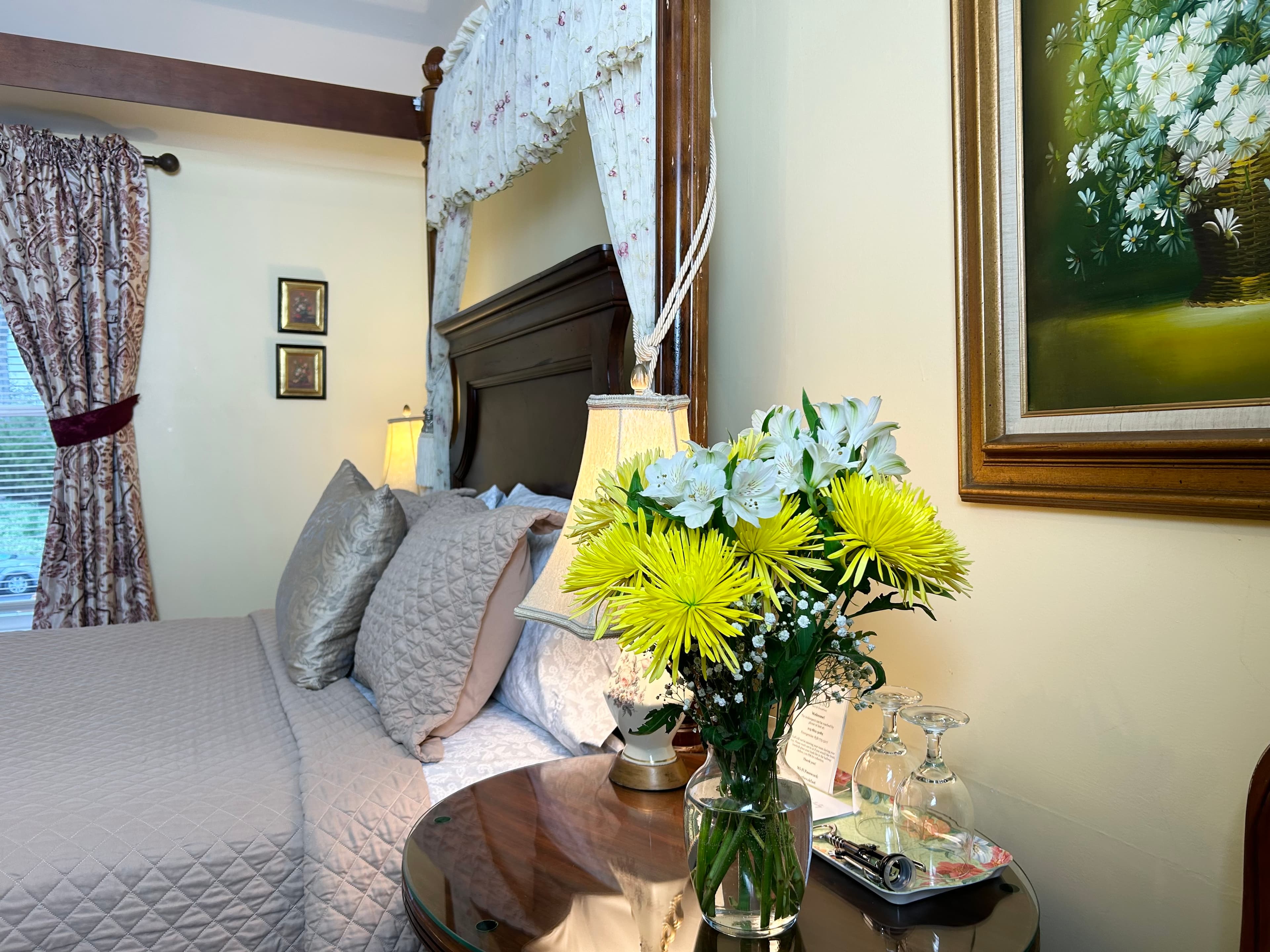 "Side view of nightstand with lamp between queen sized canopy bed and armchair"