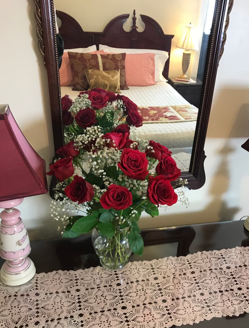 flowers and bed reflected in a vintage wood mirror with red lamp shade next to flowers