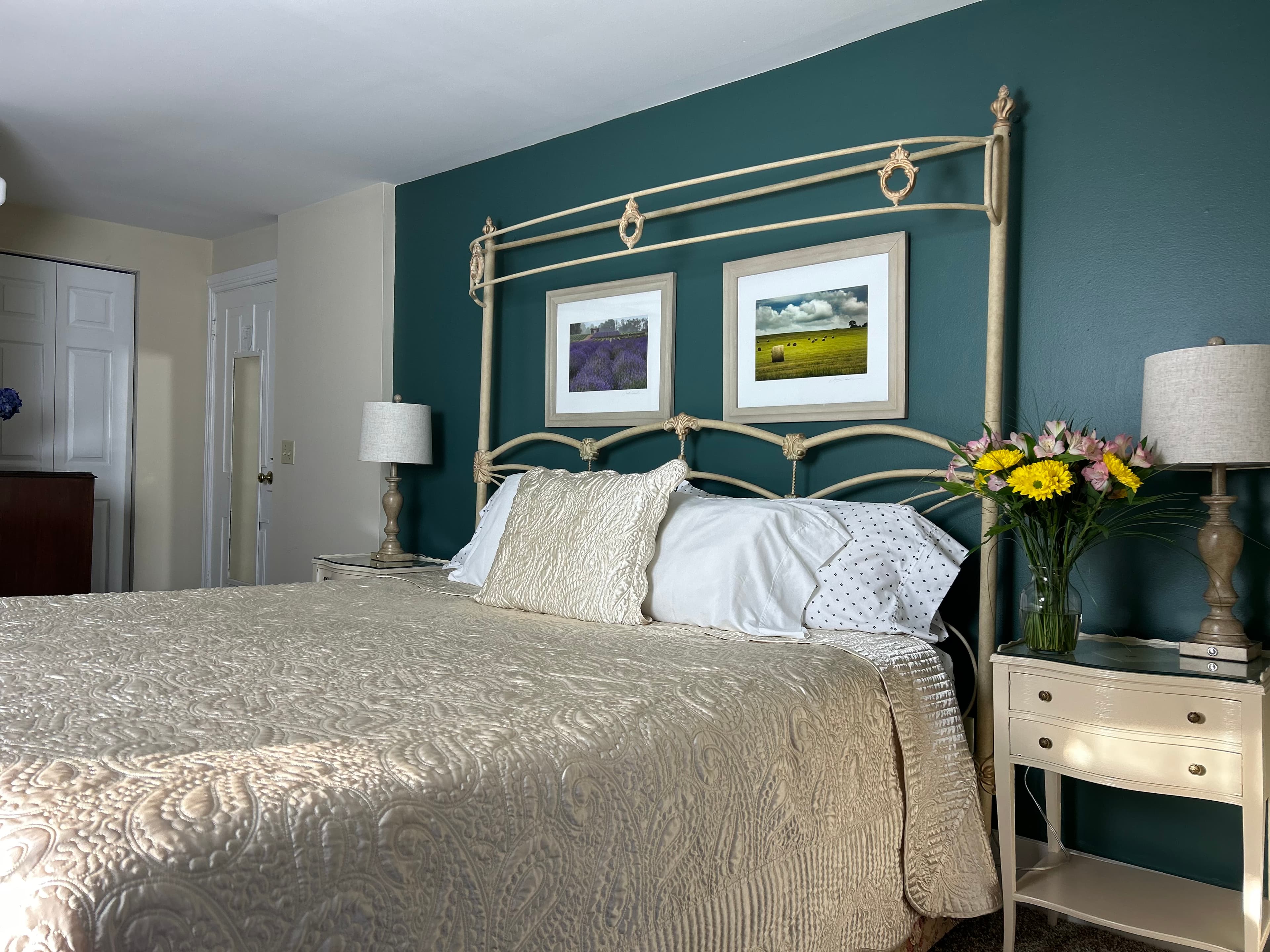 Bed, flowers in a vase on a bedside table with a lamp, door and closet