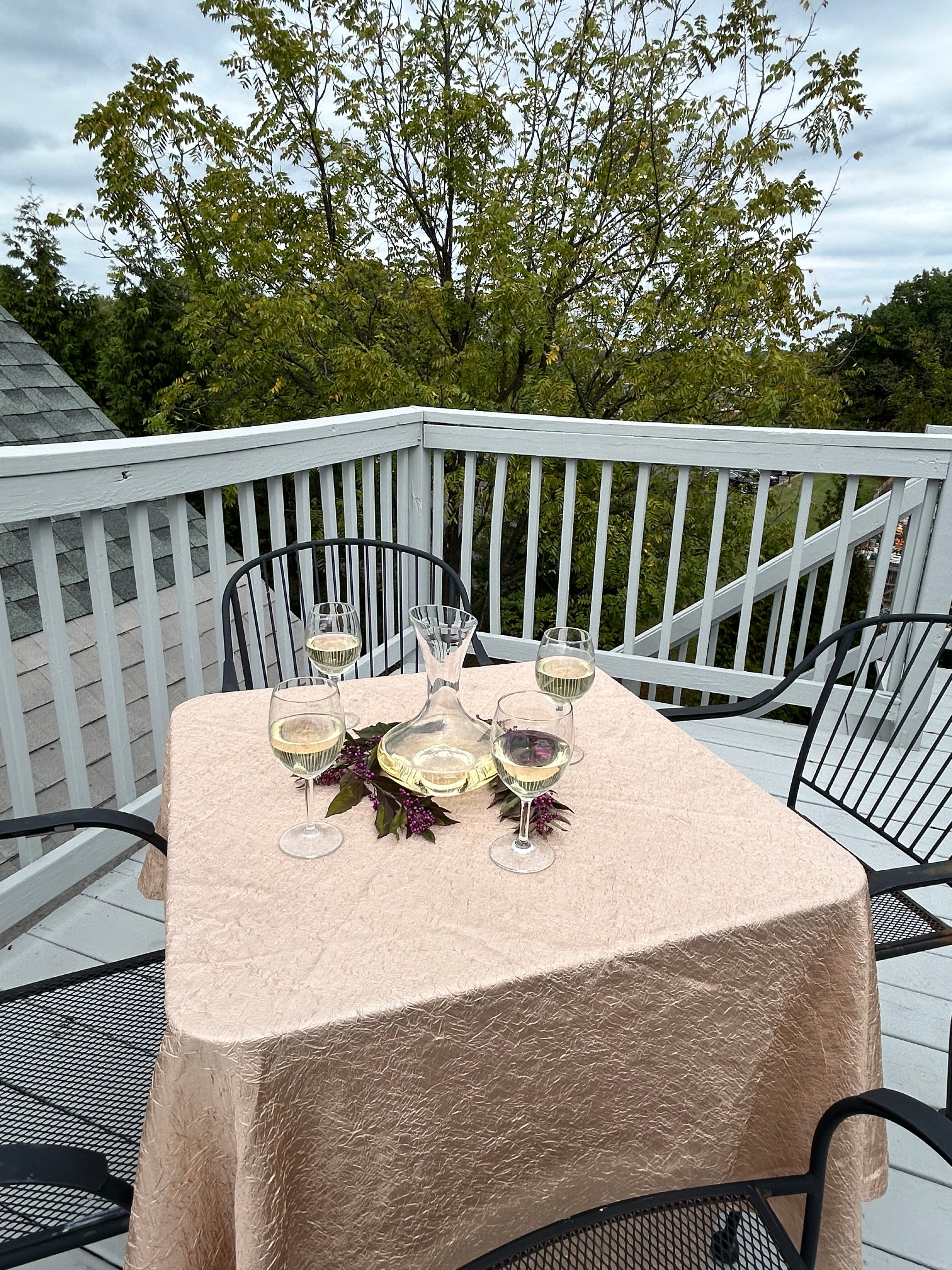 Roof top deck table with white wine and glasses overlooking green foliage