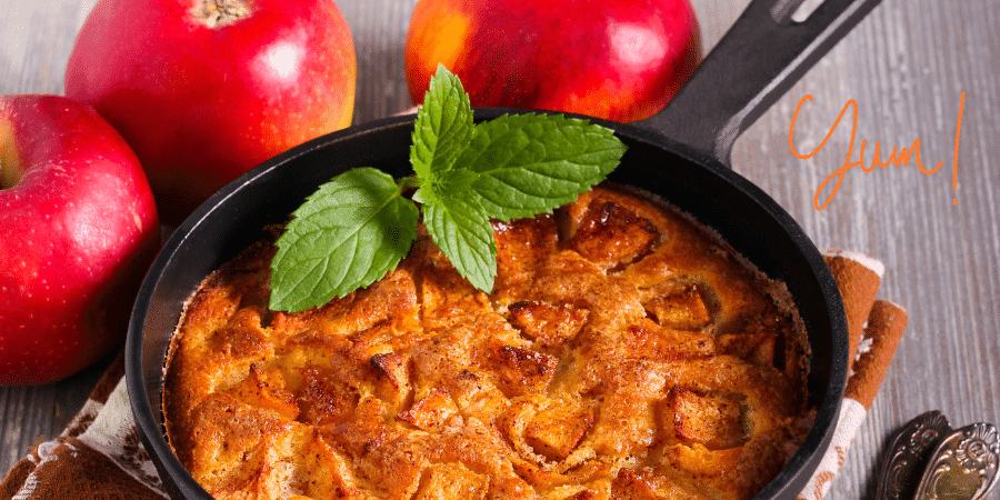 A freshly baked apple dish garnished with a mint leaf, surrounded by red apples.