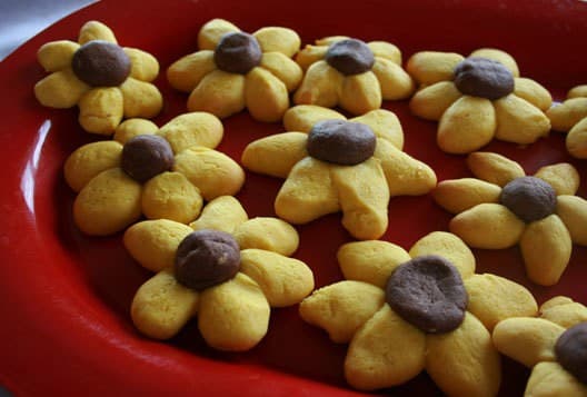 A red plate filled with yellow flower-shaped cookies with brown centers. A red plate filled with yellow flower-shaped cookies with brown centers.